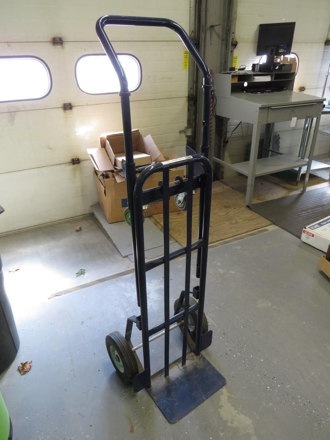 Black hand truck with two wheels in a workshop setting.