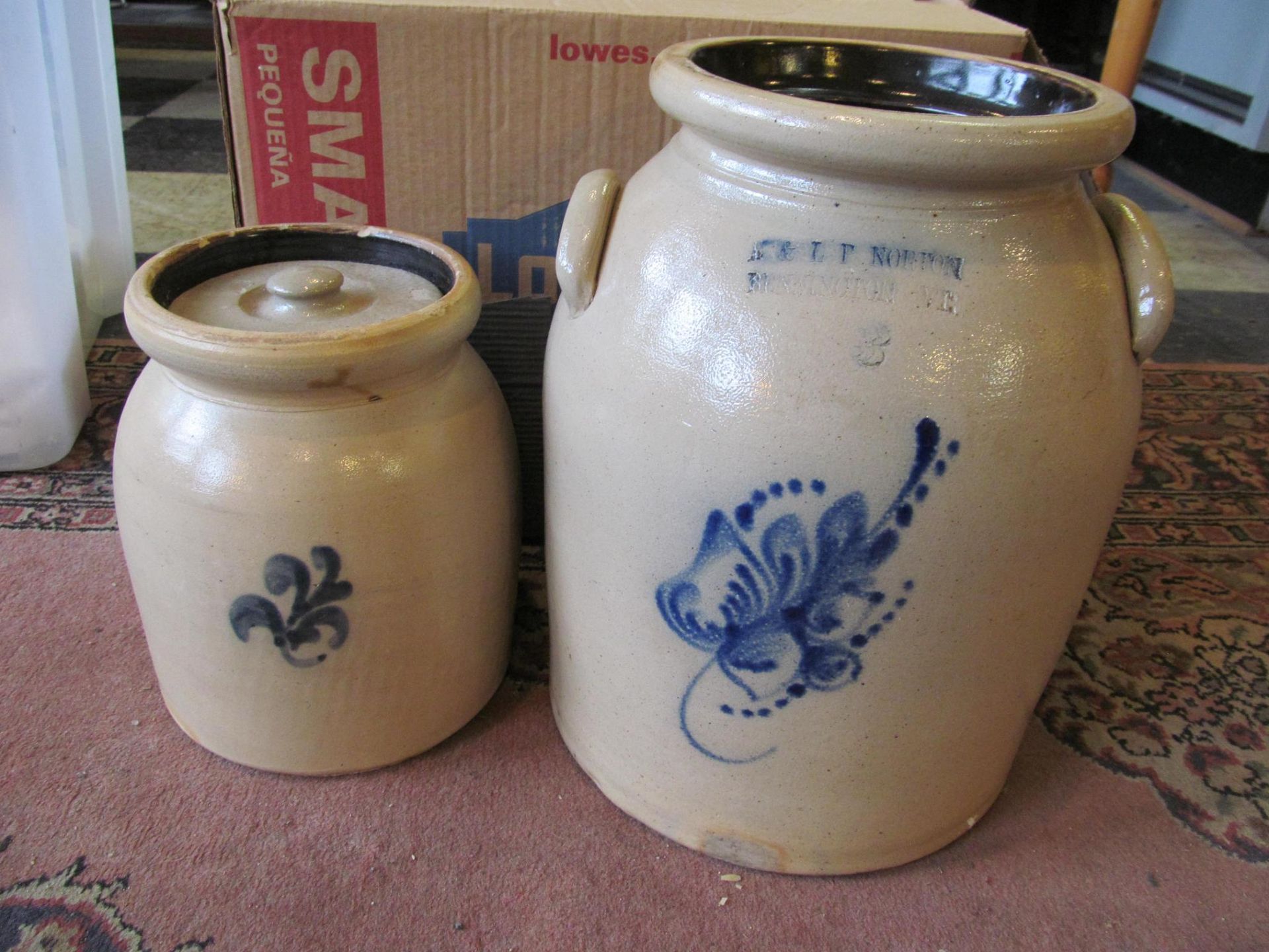Two antique stoneware jars with blue floral designs and lids.