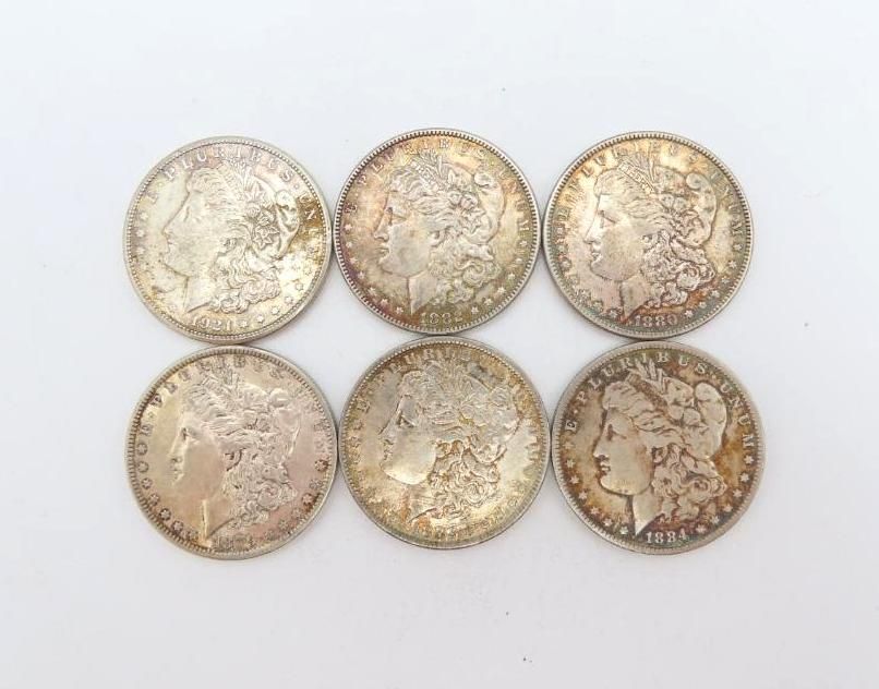 Six silver Morgan silver dollars on a white surface.