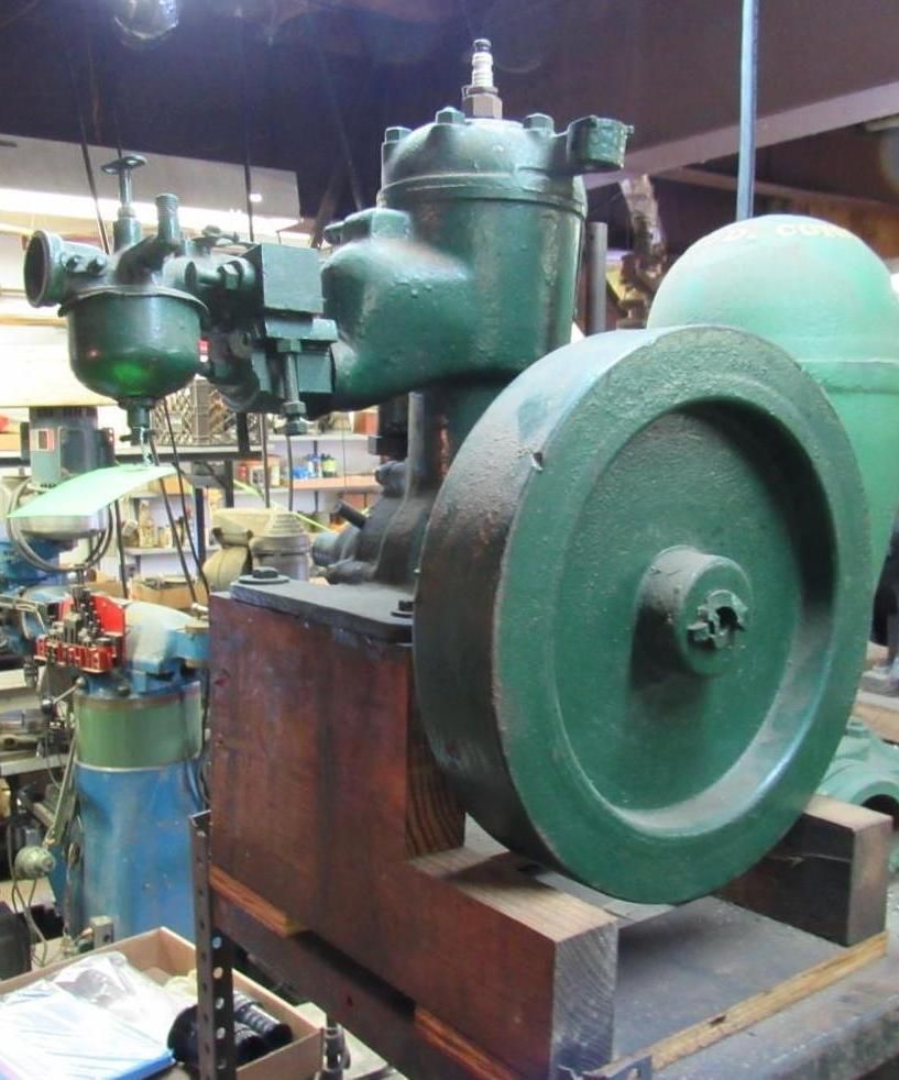 Green vintage engine on wooden base. Workshop background with tools.