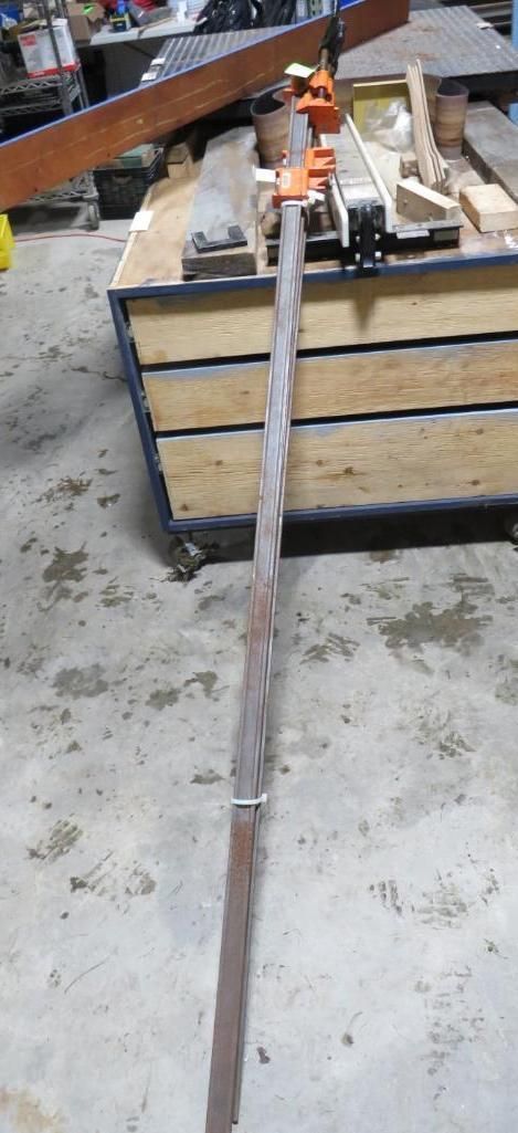 A long, metal bar held by a clamp, in a workshop setting.