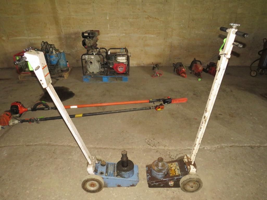 Two floor jacks with white handles and other tools in a concrete room.