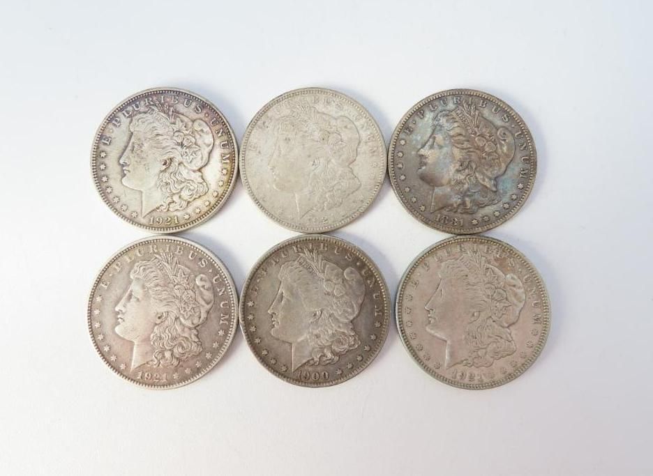 Six silver Morgan dollar coins on a white surface, each showing Liberty's profile.