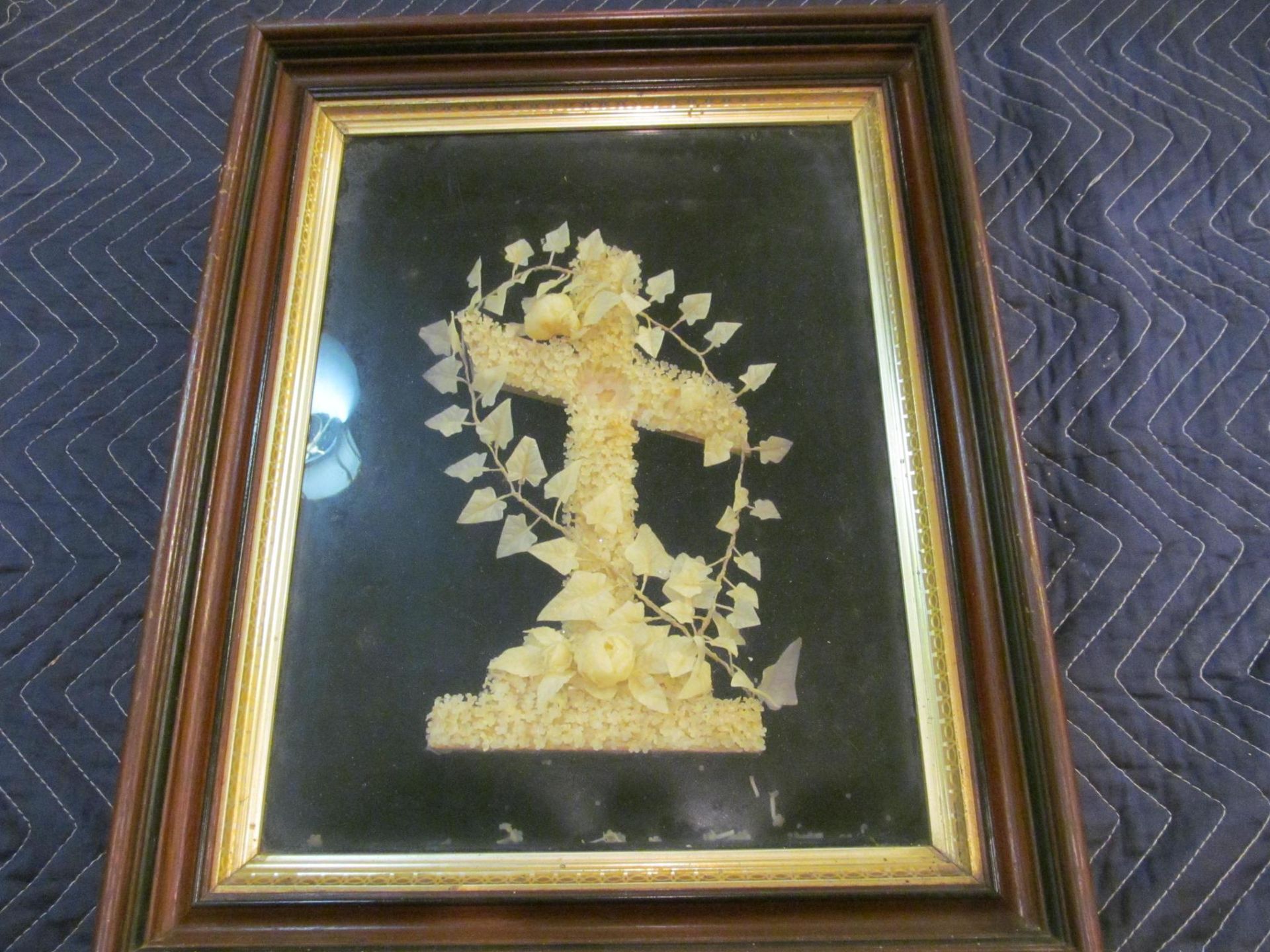 Framed artwork: Pasta cross with garland on a black background, inside a gold and brown wooden frame.