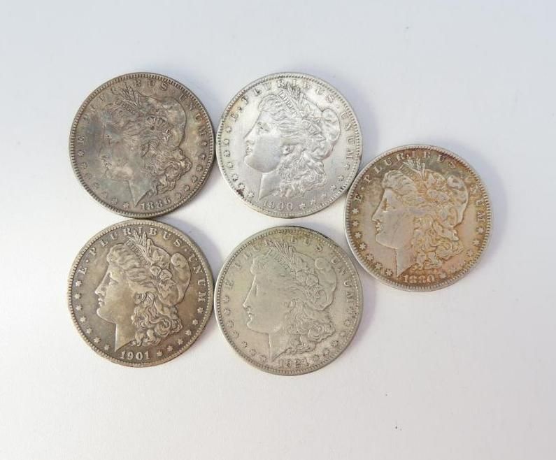 Five silver Morgan silver dollars on a white surface, showing heads.