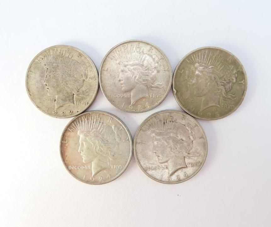 Five silver Peace dollar coins on a white surface, each showing Lady Liberty's profile.