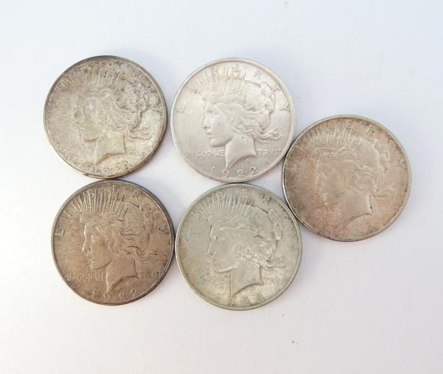 Five silver Peace dollar coins on a white surface, showing profiles of a woman.