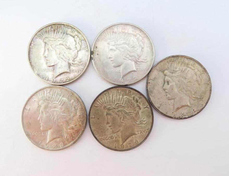 Five silver Peace dollar coins on a white surface.