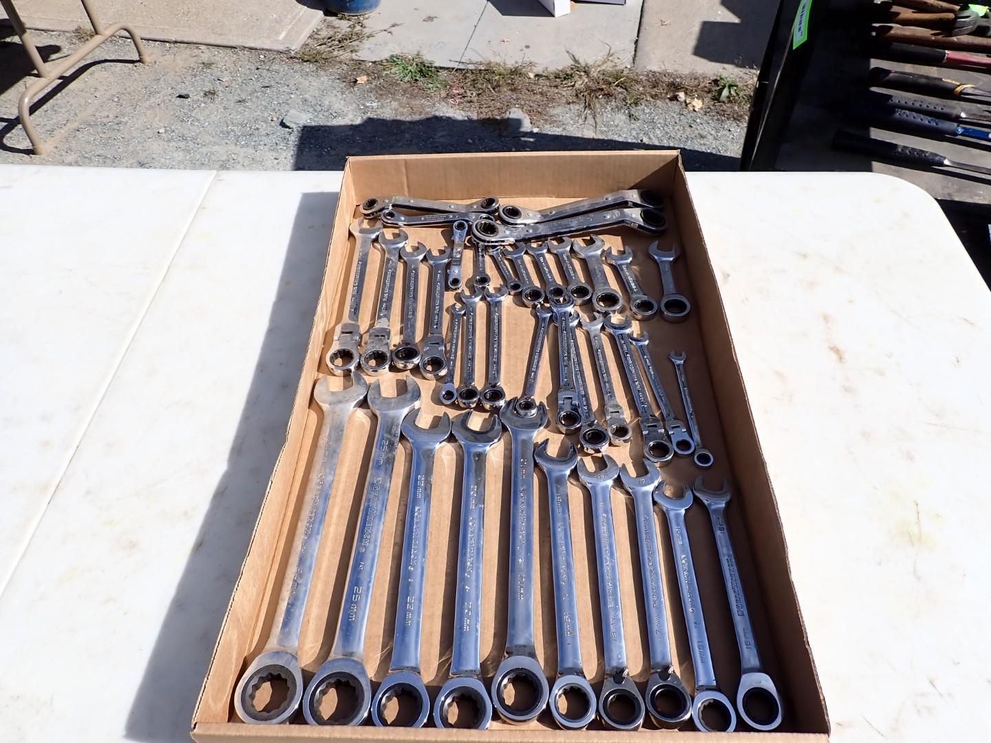 Cardboard box filled with assorted chrome combination wrenches on a sunlit outdoor table