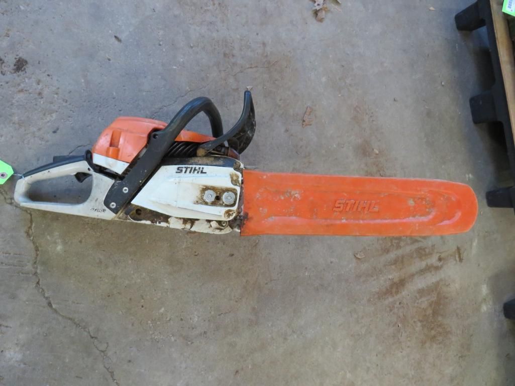 Stihl chainsaw, orange and white, lying on concrete.