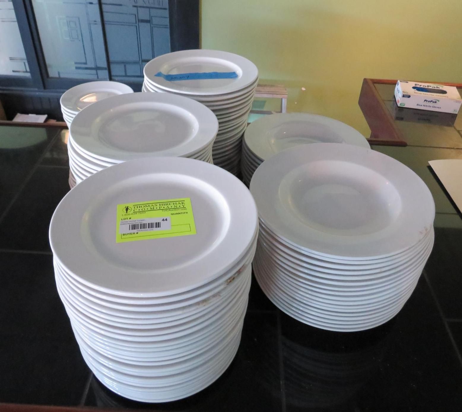 Stacks of white plates on a black table with a bright yellow sticker on one.