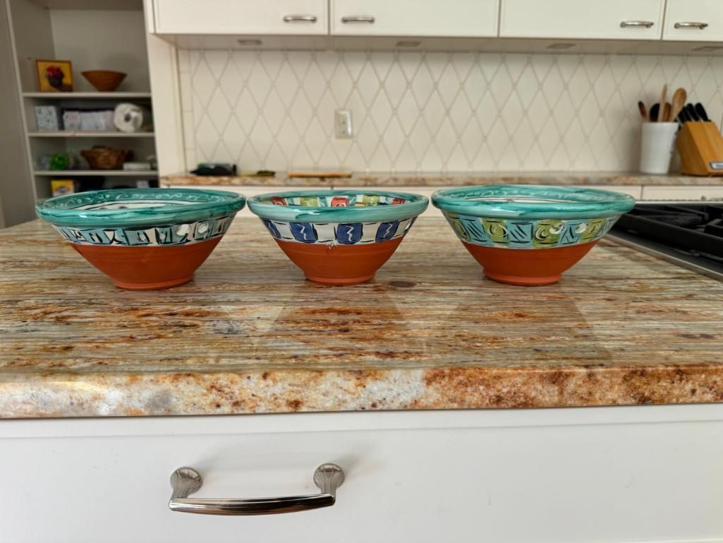 Three decorative ceramic bowls on a countertop. Turquoise and orange colors. Kitchen in the background.