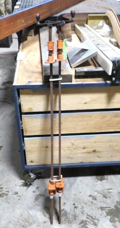 Two pipe clamps with orange ends, resting vertically against a workbench.