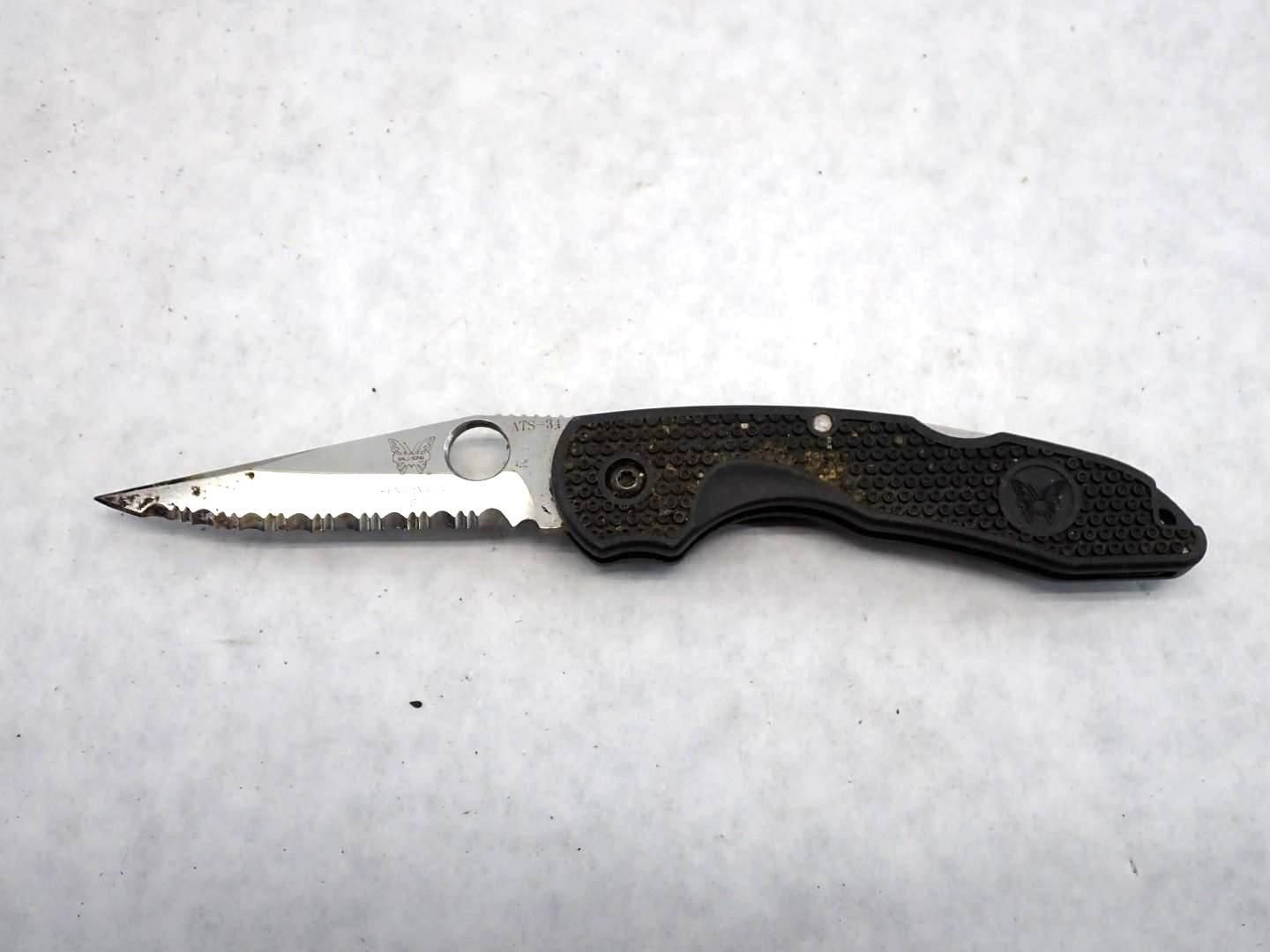 A Spyderco serrated folding knife with a black handle, lying on a white surface.