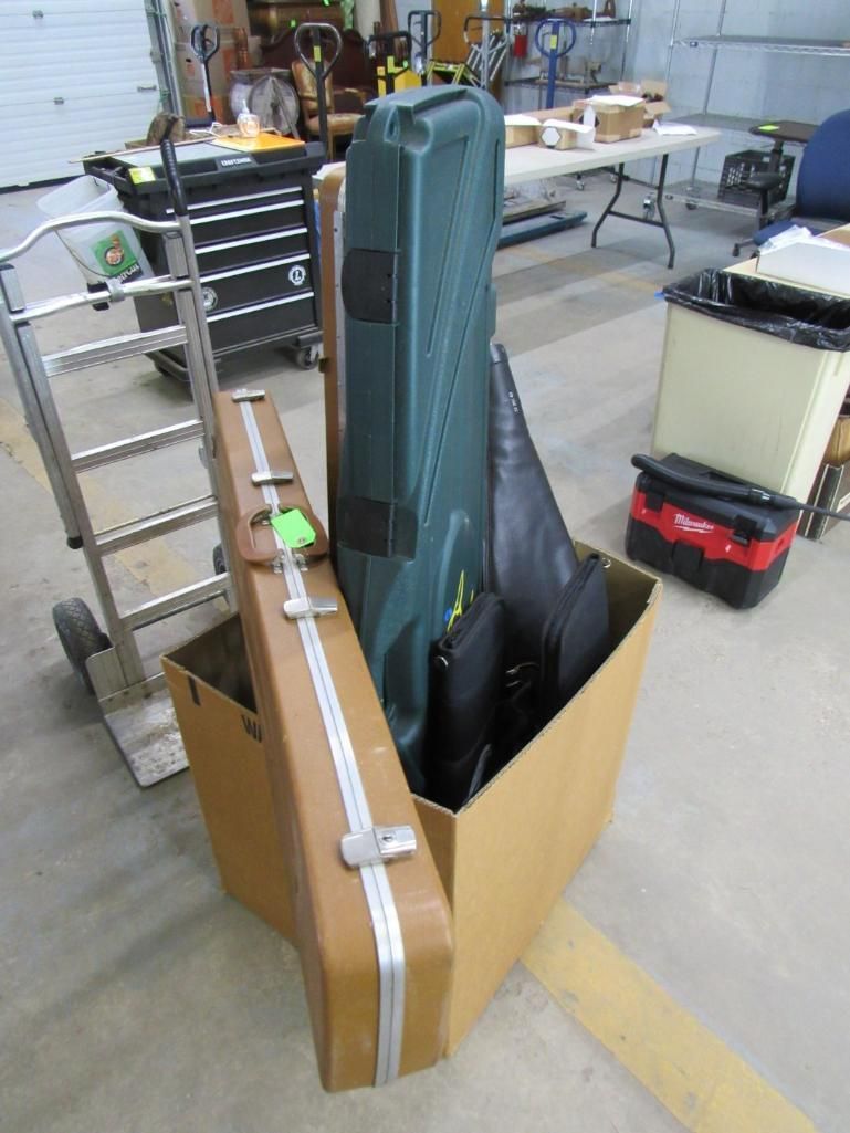 Cardboard box filled with a brown guitar case, a green hard case, and other items. In a workshop setting.