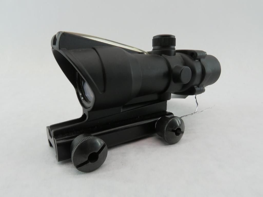 Black rifle scope with a built-in mount, featuring adjustable knobs and lens.