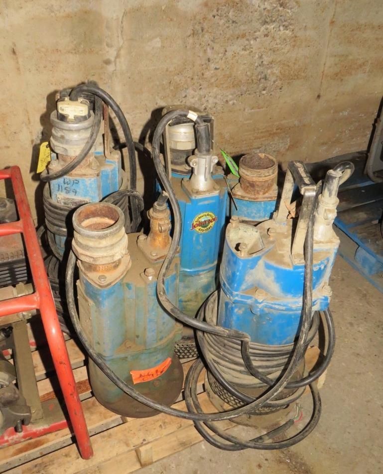 Four blue submersible water pumps on a wooden pallet in a storage area.