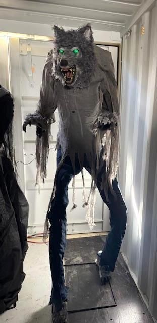 Werewolf Halloween decoration with green glowing eyes, tattered shirt, and blue jeans.