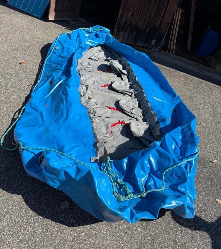 Blue inflatable boat sitting outdoors on pavement. Rope drawstring visible.