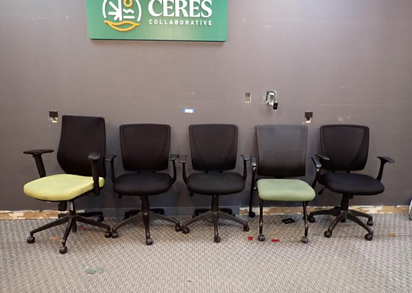 Five office chairs in a row against a gray wall, two with green seats.