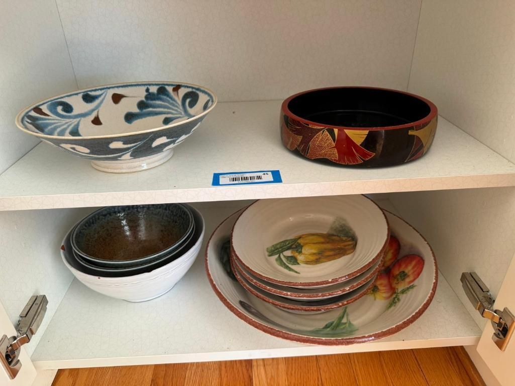White cabinet with two shelves holding various bowls and plates in blue, brown, and floral designs.