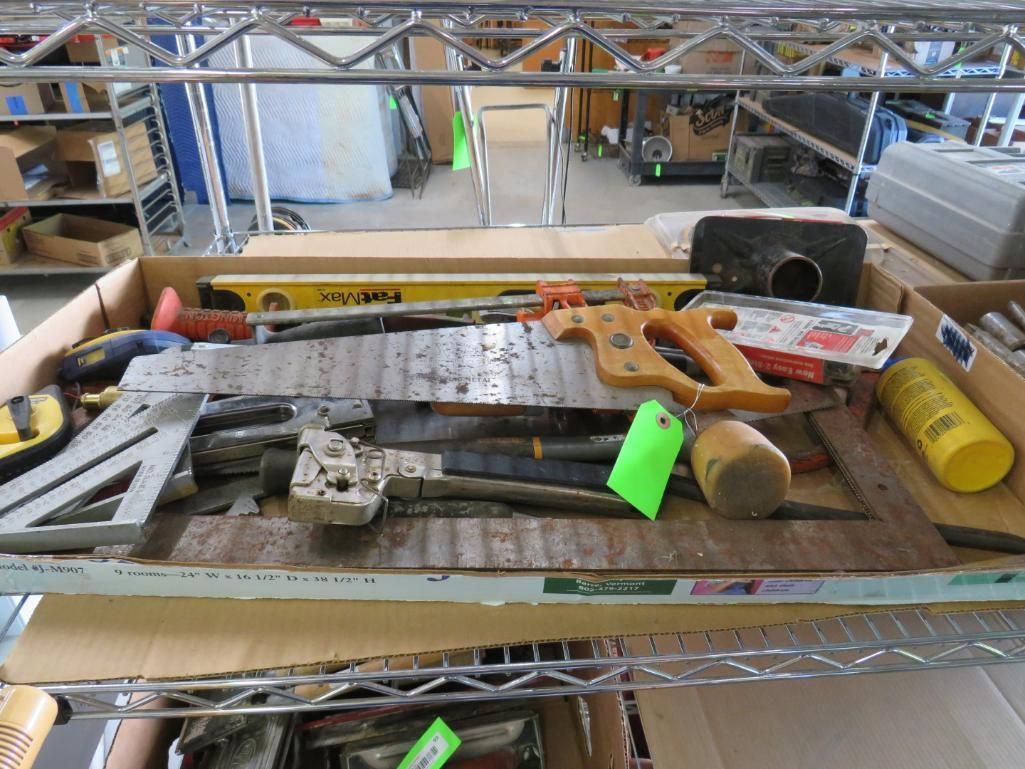 Tools in a cardboard box on a metal shelf, including saws, levels, and mallets.