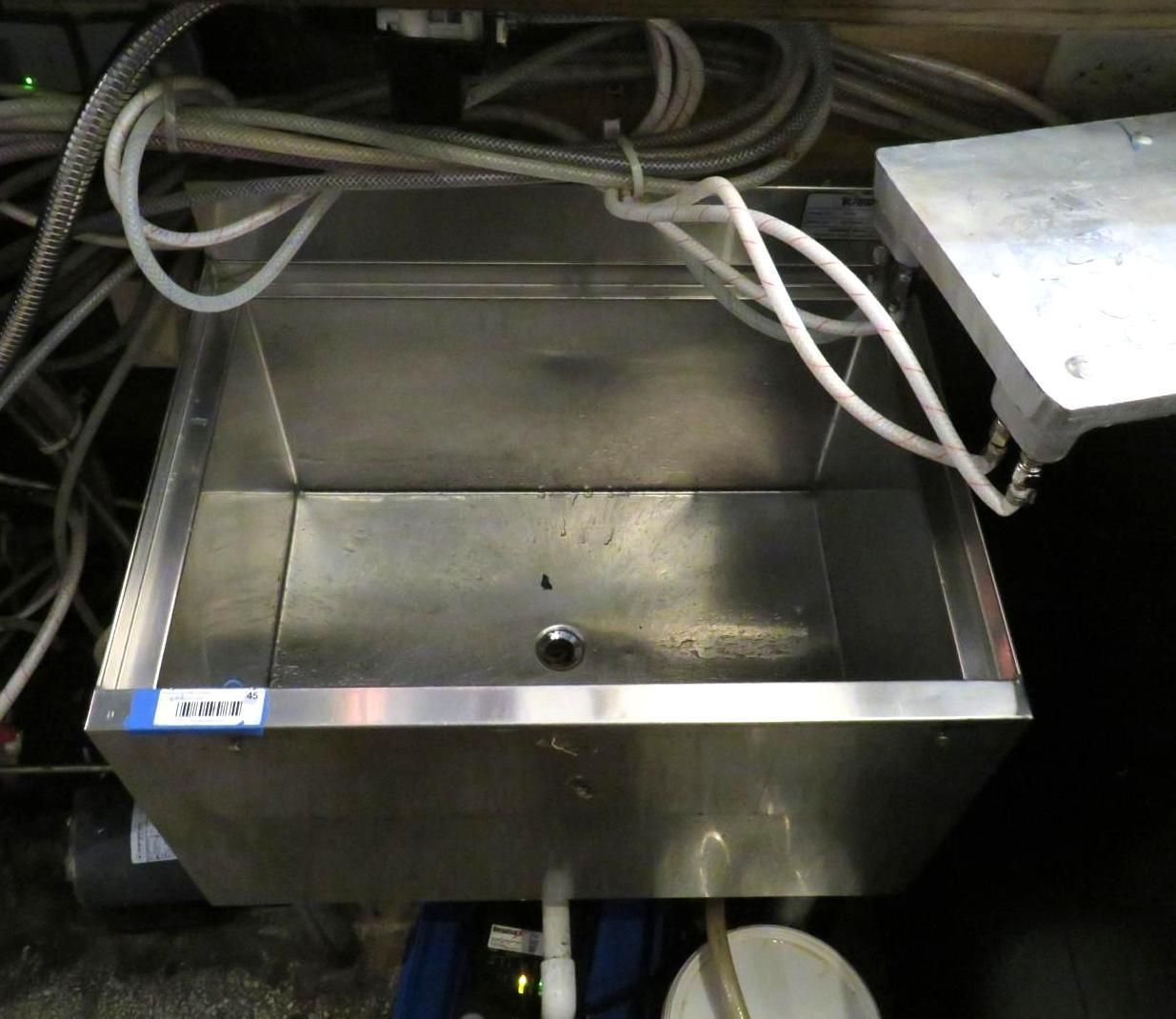 Stainless steel sink with plumbing and hoses in an industrial setting.