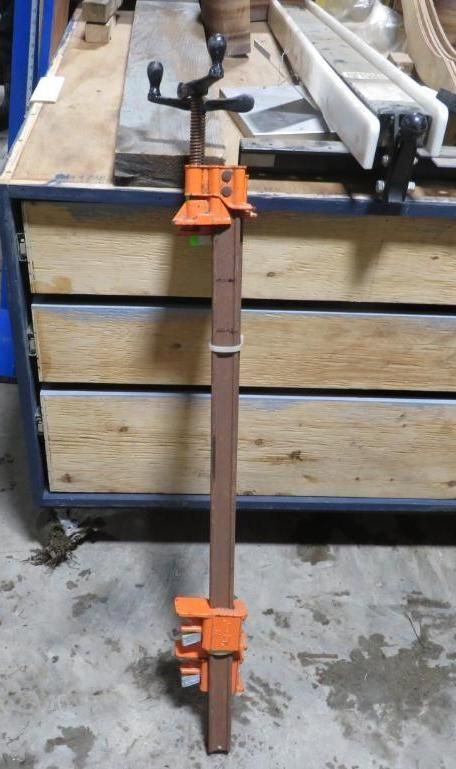 Orange and brown bar clamp on a wooden surface, ready for use.