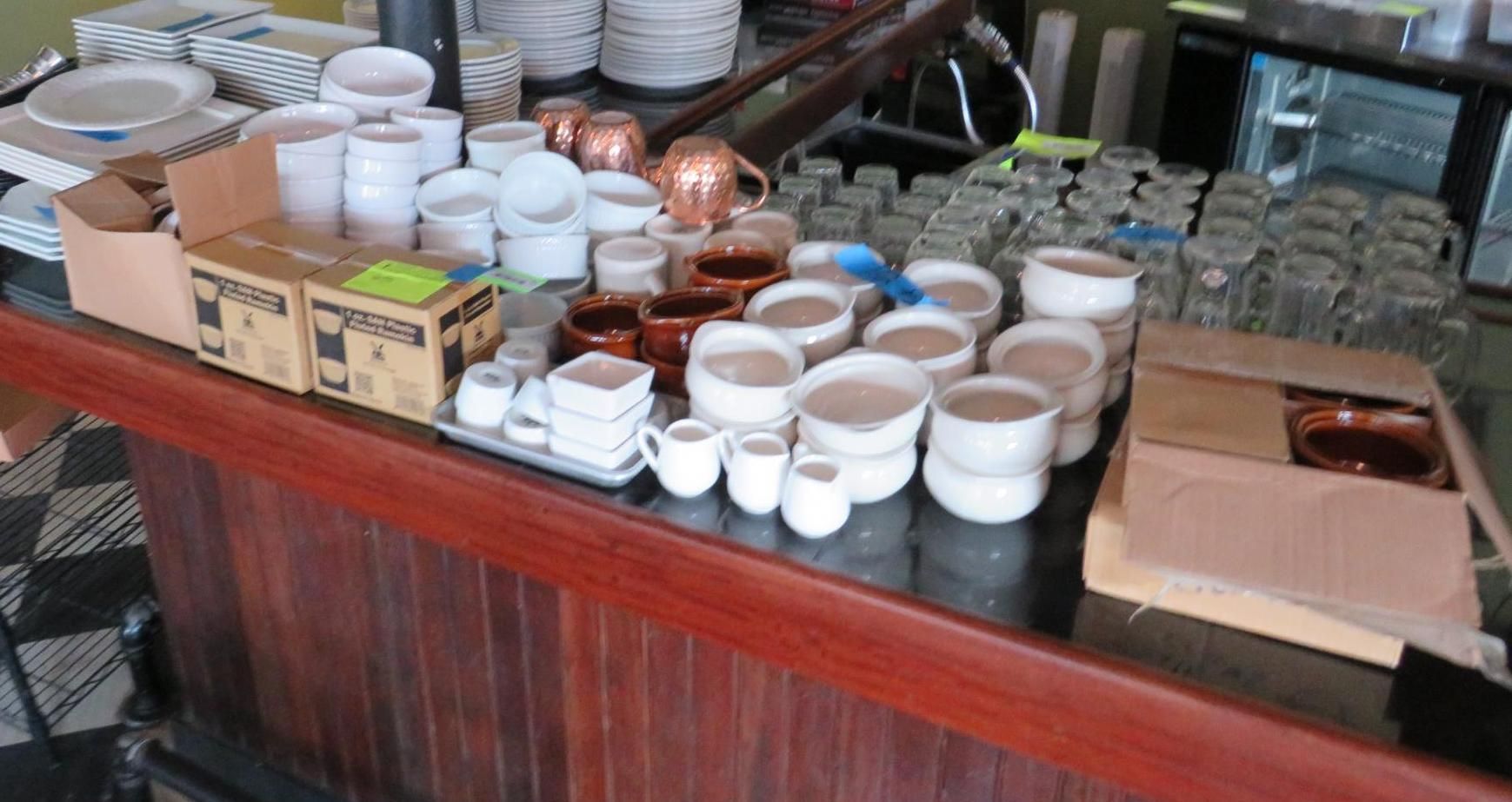 Restaurant bar with stacks of dishes, glasses, and copper pots on a wood counter.