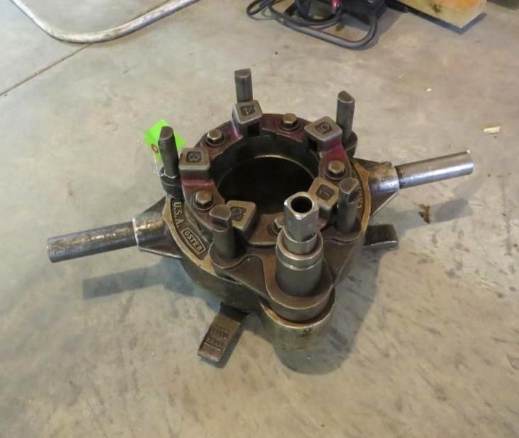 A large metal pipe threading tool on a concrete surface.