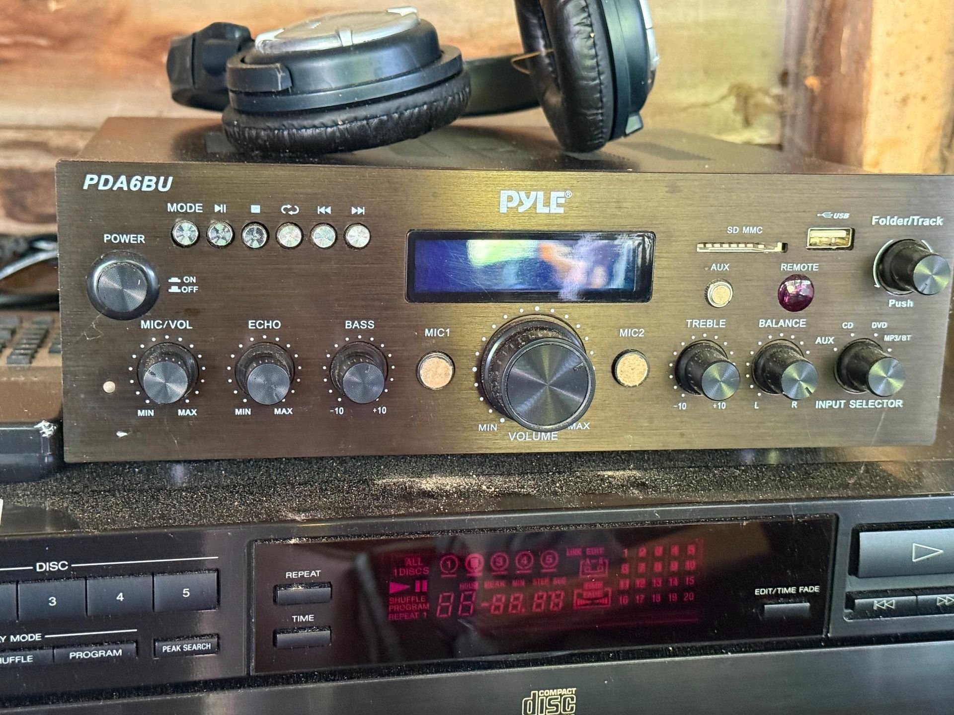 Bronze audio receiver with knobs and display, headphones on top, sitting atop a CD player.