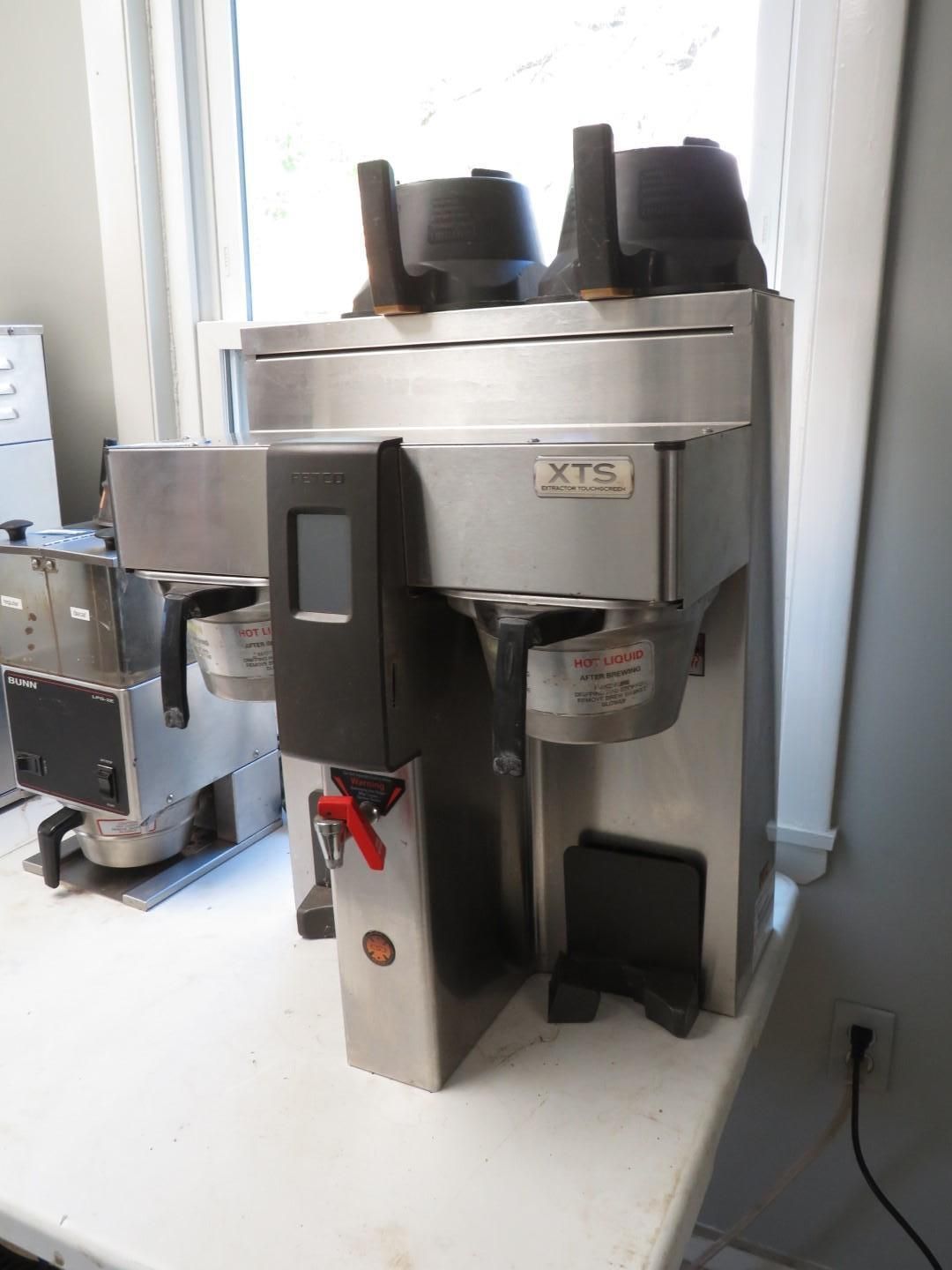 Stainless steel commercial coffee machine with two brewing stations, next to a window.