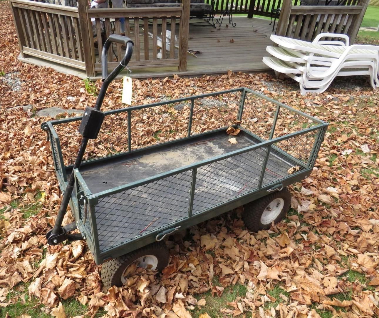 Green metal utility wagon with a mesh sides, sitting on fall leaves.