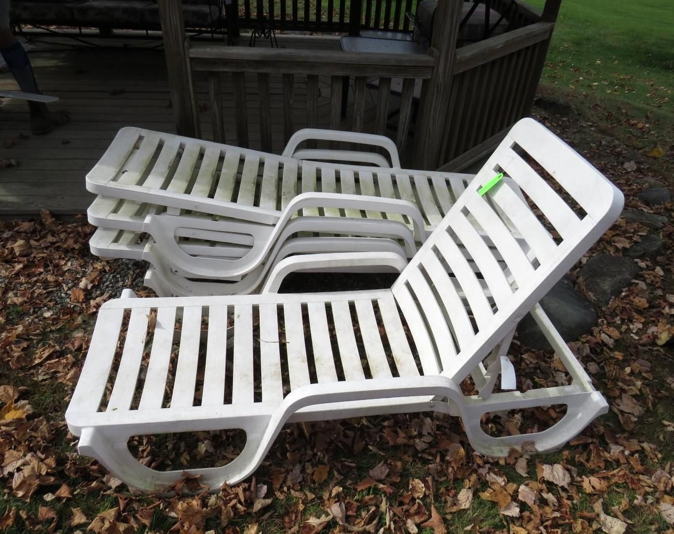White plastic lawn chairs stacked outdoors near a wooden gazebo.