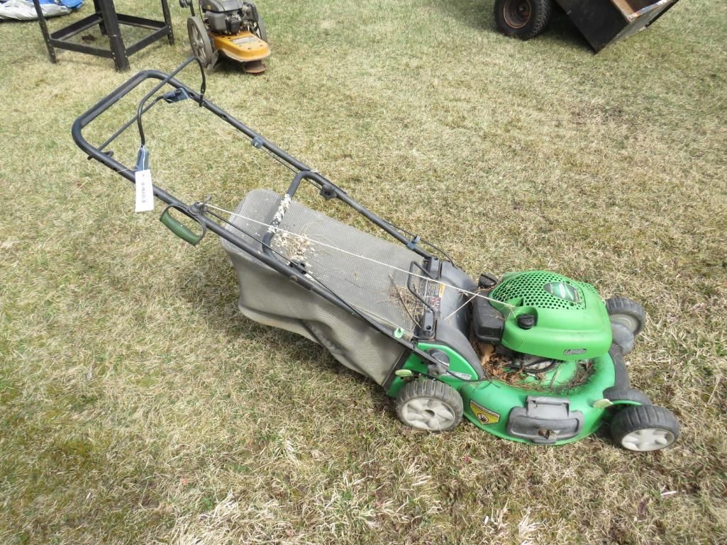 Green lawnmower on grass; a bag is attached.