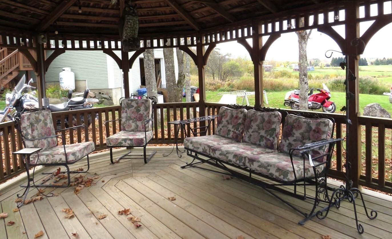 Gazebo with outdoor furniture on a wooden deck, overlooking a yard with fall foliage.