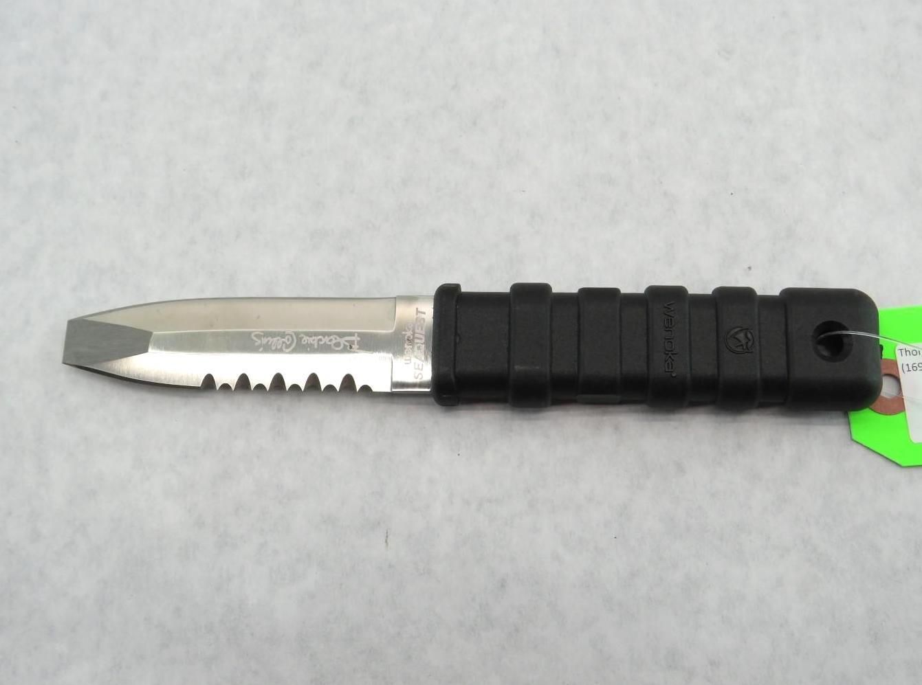 Black handled diving knife with serrated edge on a light gray surface.
