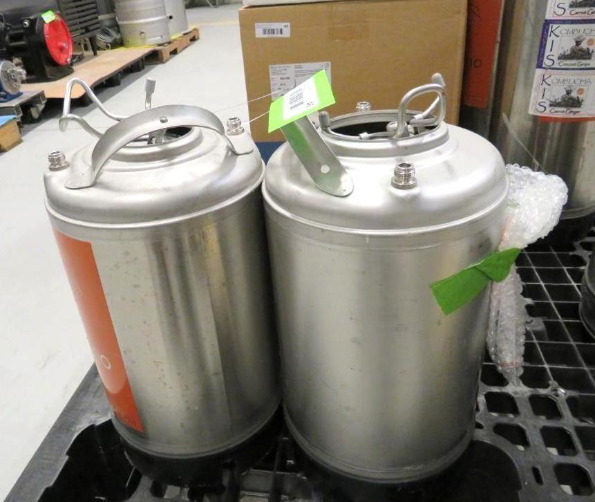 Two stainless steel kegs with handles, sitting on a black pallet indoors.