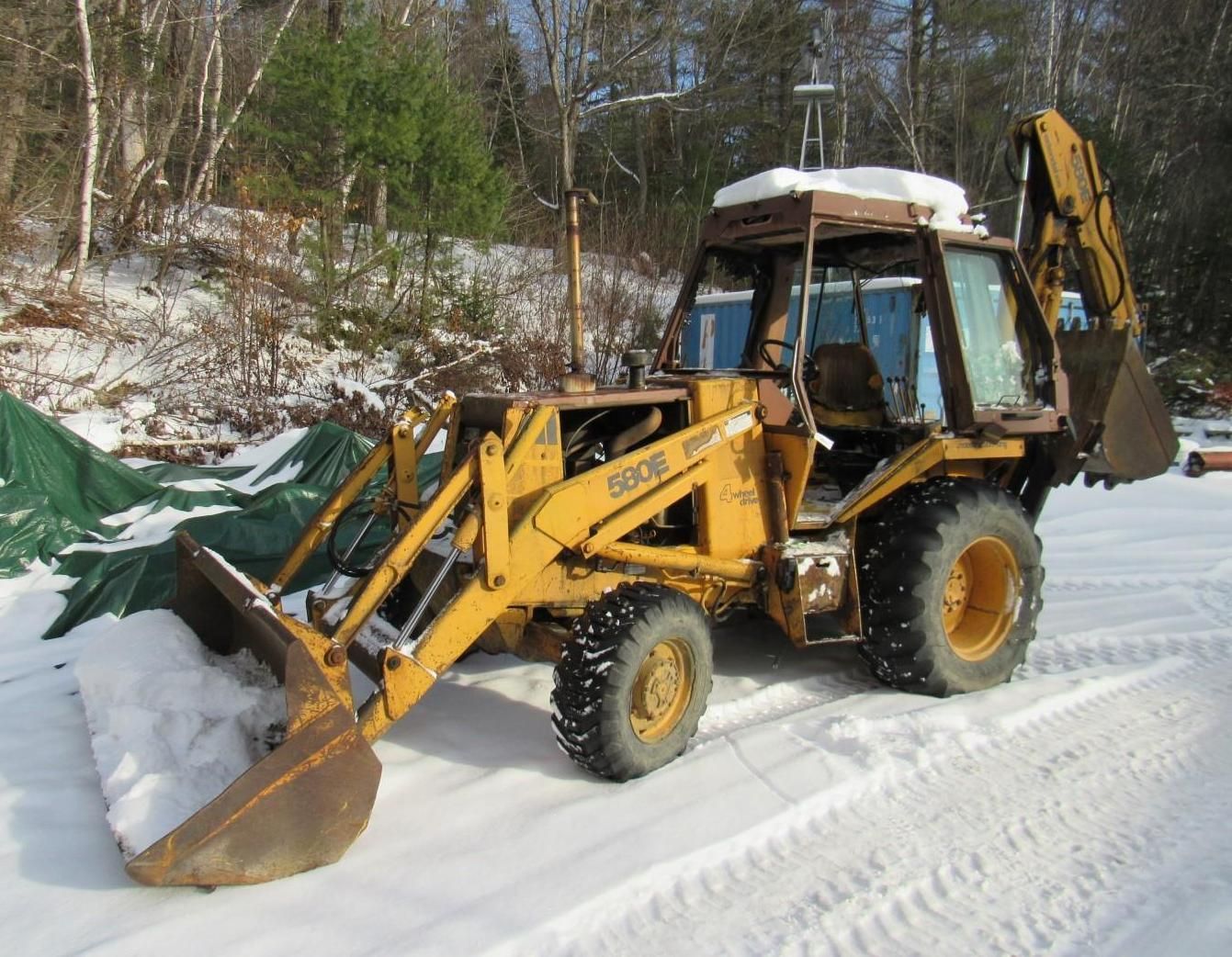 Yellow Case 580 Super E Backhoe parked in snow; forested background.