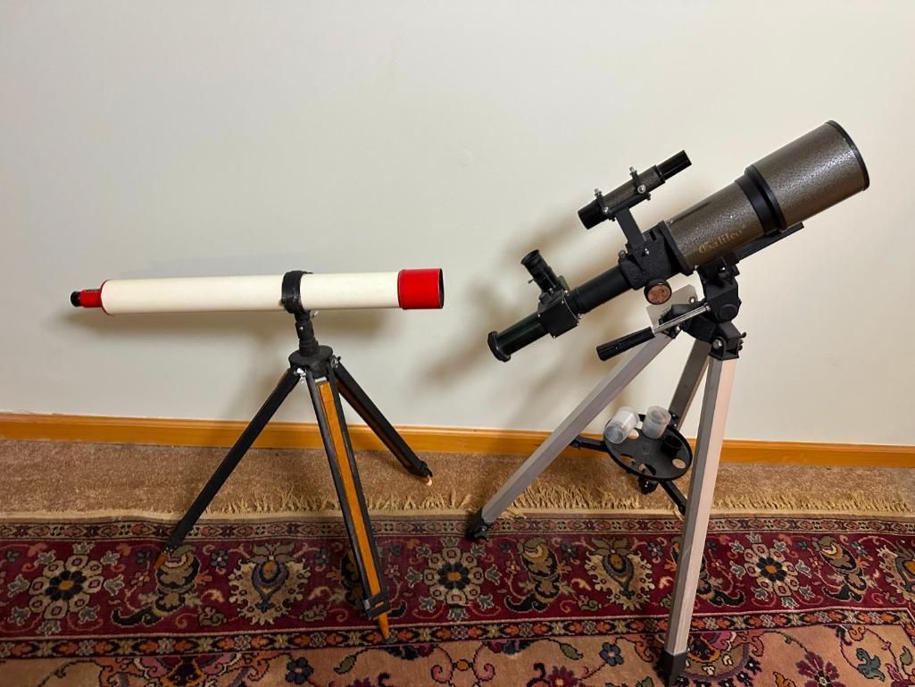 Two telescopes on tripods, one white and red, the other brown and black, against a wall and rug.