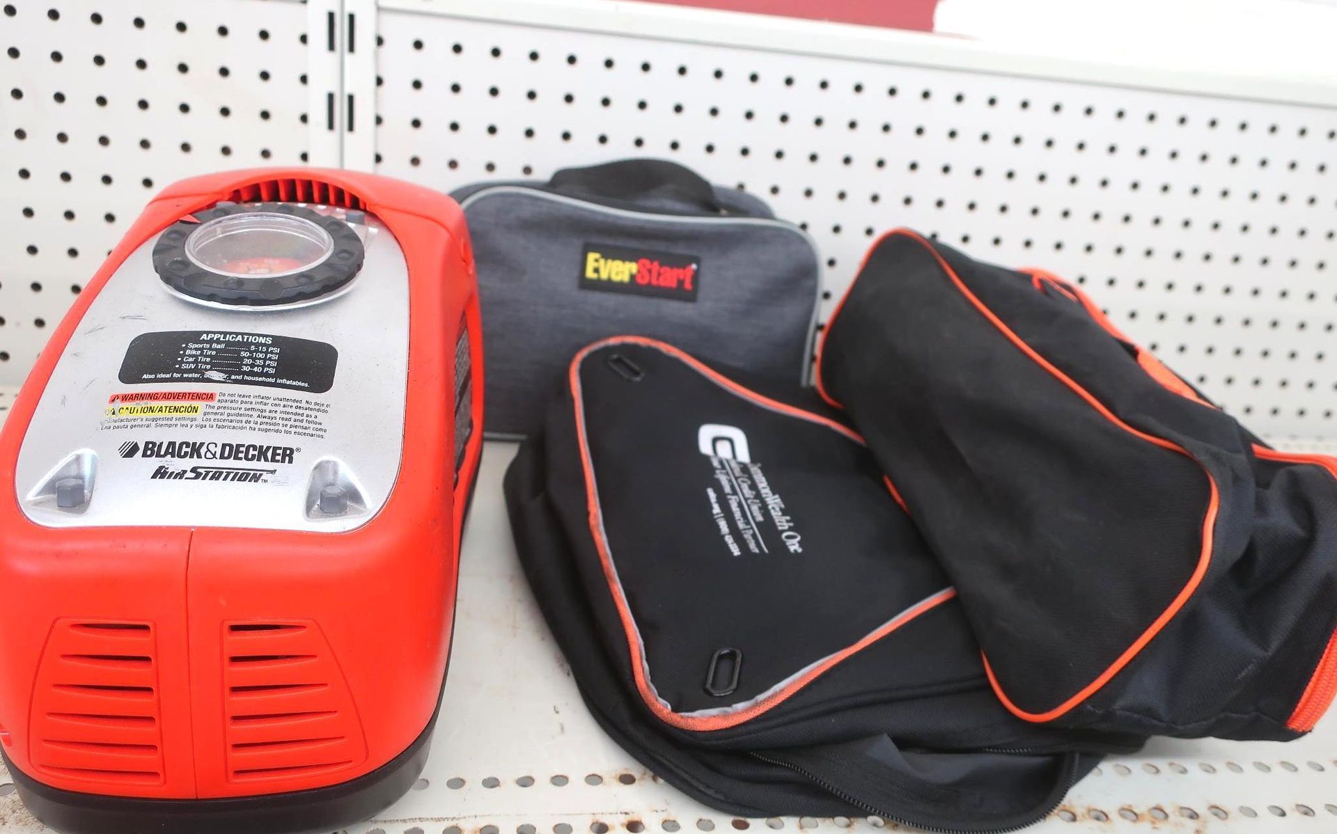 Red and silver air compressor, two black bags, and a gray bag on a store shelf.