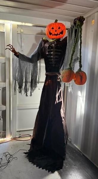 Animated Halloween decoration: jack-o'-lantern head, skeletal body, holding pumpkins, standing in a doorway.