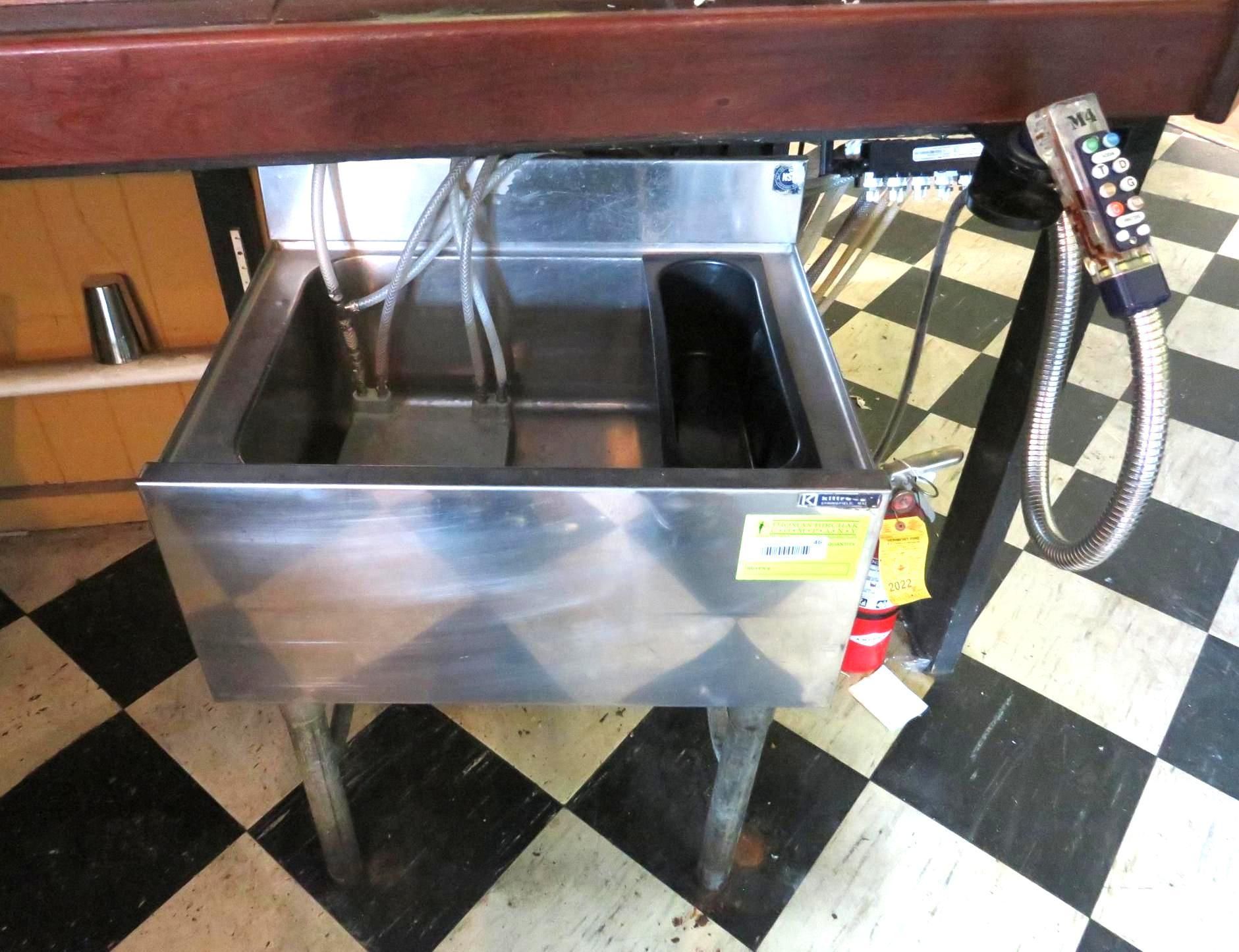 Stainless steel bar sink with two basins and attached plumbing.