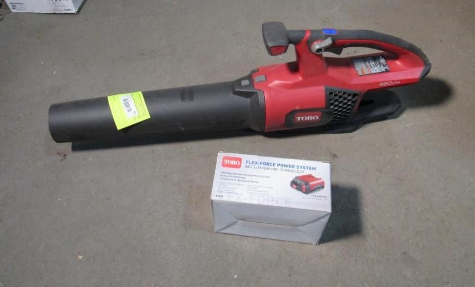 Red and black cordless Toro leaf blower with a battery box on a gray surface.