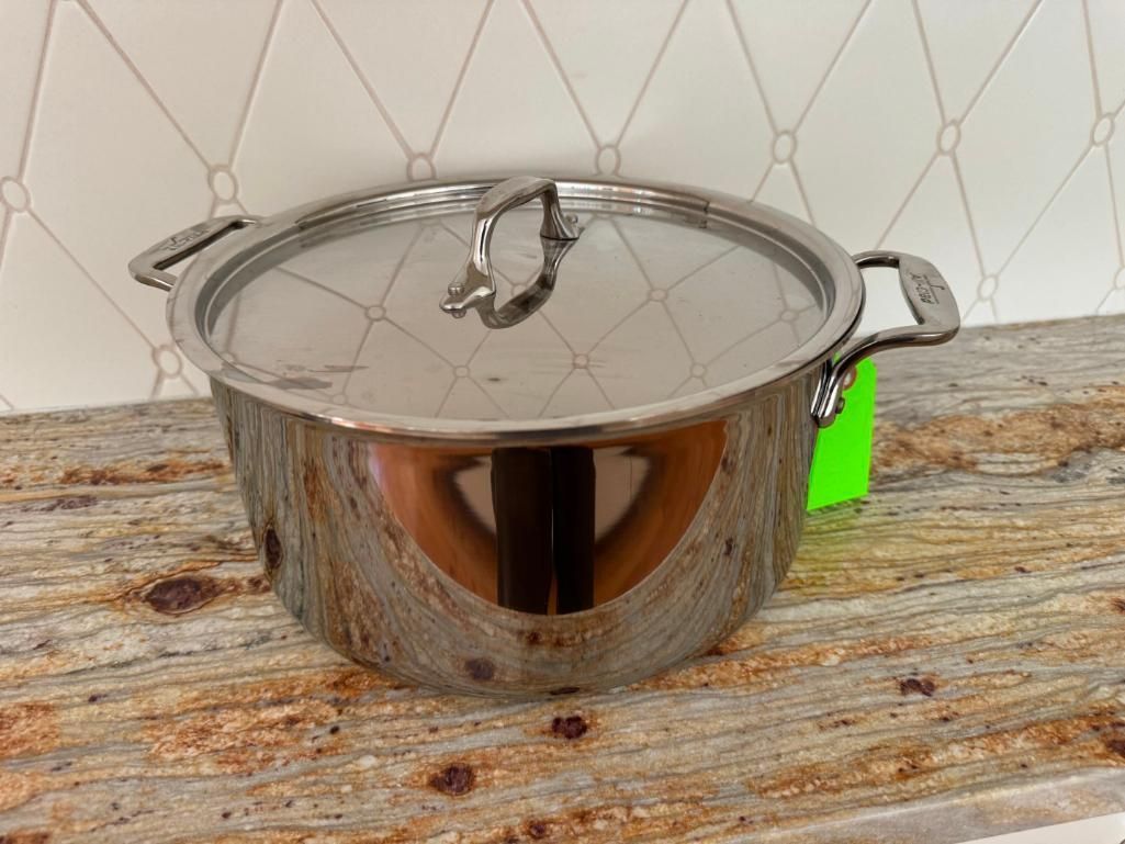 Stainless steel pot with lid on a granite countertop, next to a tiled wall.