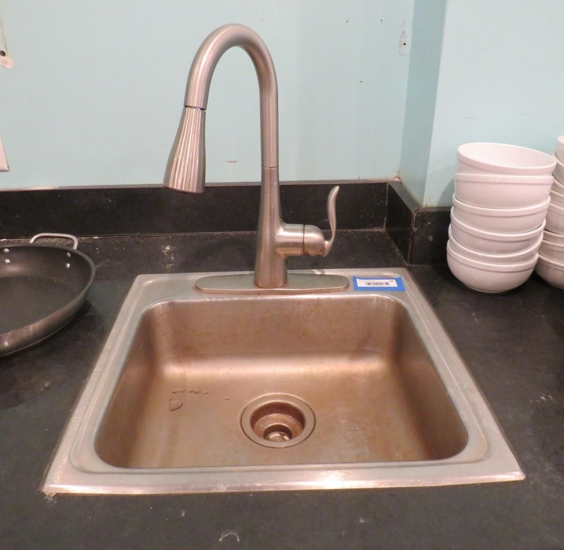 Stainless steel sink with faucet, bowls, and pan on a black countertop.