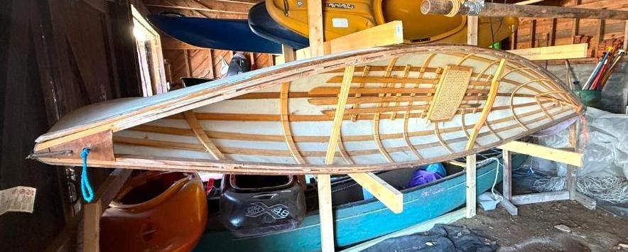 Wooden canoe frame in storage, supported by wooden stands.