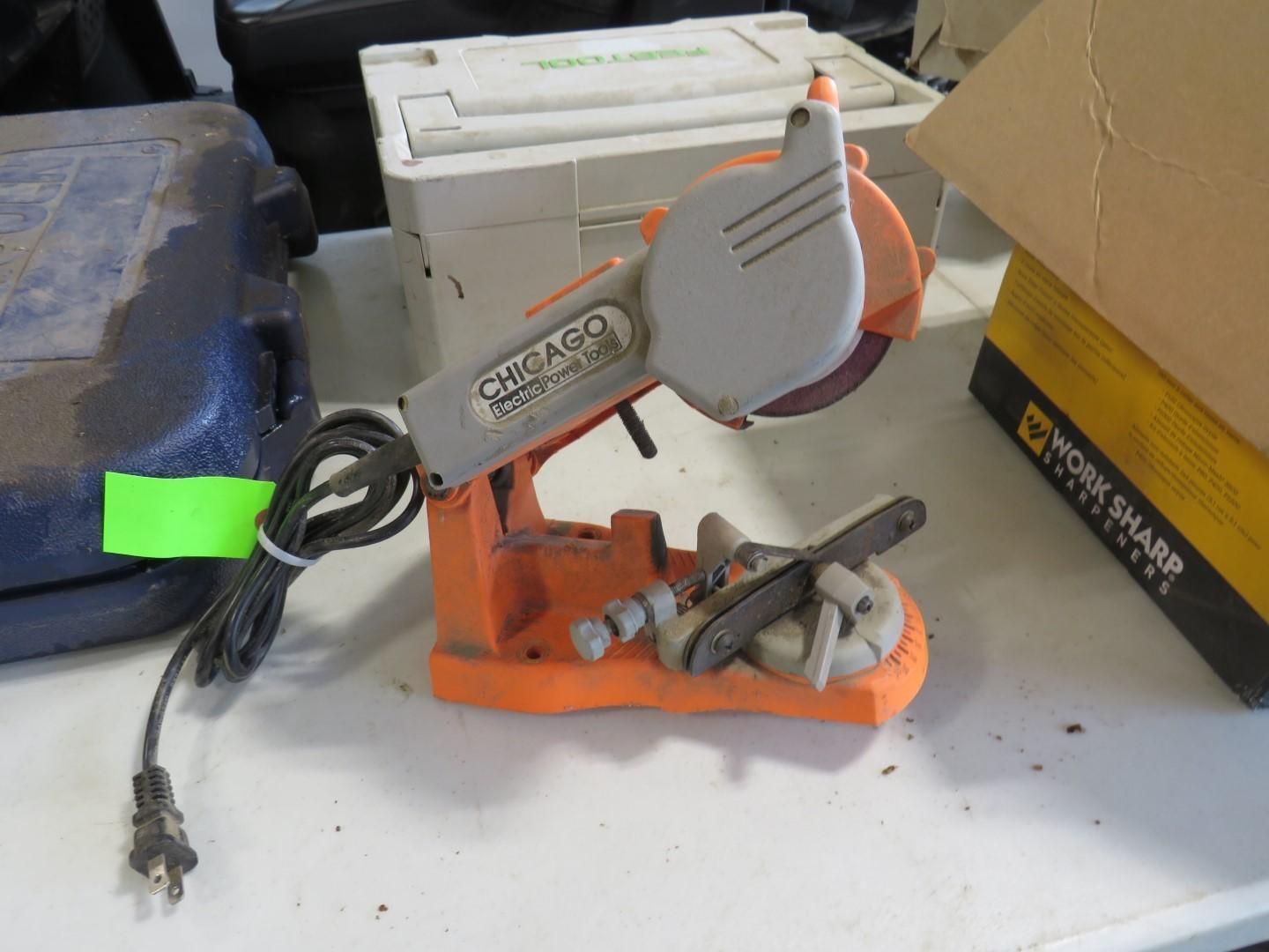 Orange and gray Chicago electric chainsaw sharpener with grinding wheel, power cord, on a white table.