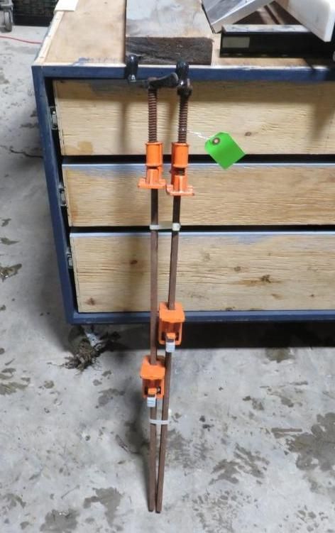 Two copper pipes with orange clamps, standing upright against a wooden structure.
