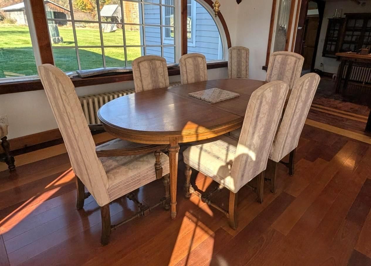 Dining table with six upholstered chairs by large windows in a sunlit room